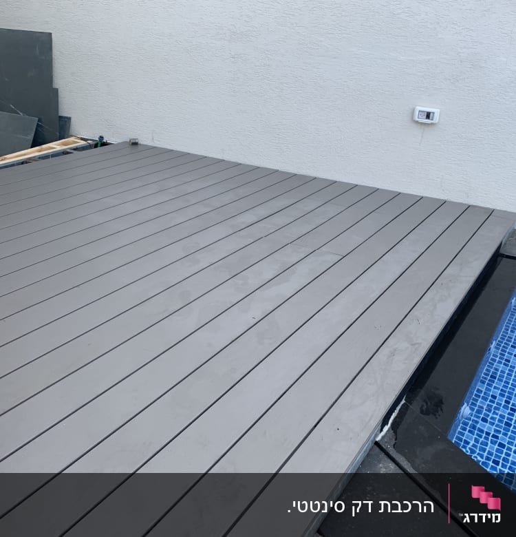 דק עץ ליד בריכה עם אריחים כחולים